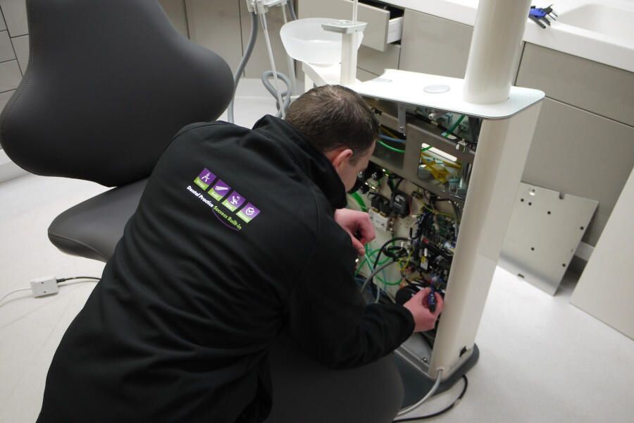 Technician repairing or assembling machinery inside a dental office, with wires and components visible.