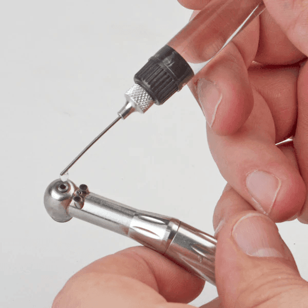 Hands holding dental drill and syringe, showing maintenance or repair process.