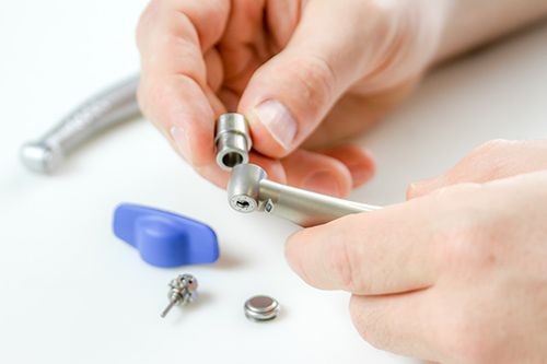 Person holding a dental handpiece with tools and components on a white surface.