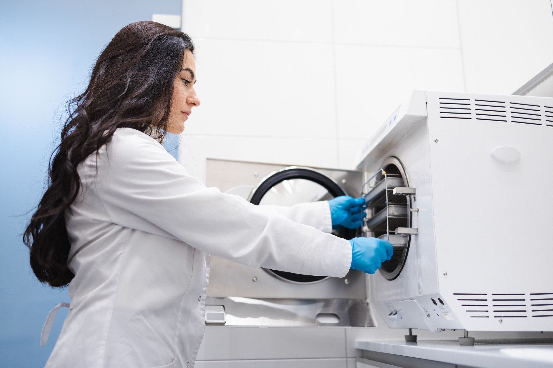 Female medical assistant is taking out pockets with sterilized dental instruments from autoclave